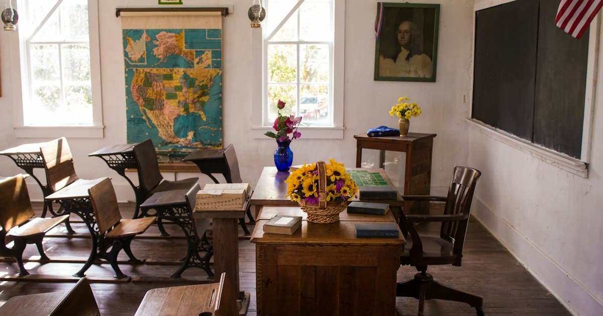 An old-fashioned classroom with wooden desks, a map of the United States and an American flag.